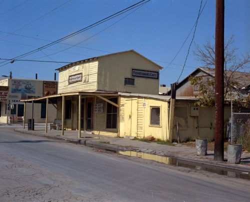 A yellow building with an awning over the sidewalk and signs on the front and side that say Fisherman's Cafe.