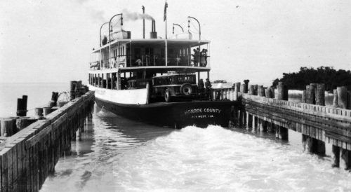 A two-level ferry boat pulling out of a landing with railings on either side.