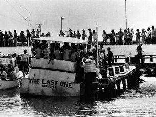 A crowd of people standing on a dock and on a boat with the name The Last One, Miami, Fla written on the stern.