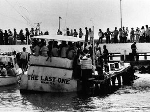 A crowd of people standing on a dock and on a boat with the name The Last One, Miami, Fla written on the stern.