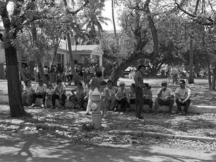 A group of people sitting on a low wall in front of a building with a group of people standing in front of it.