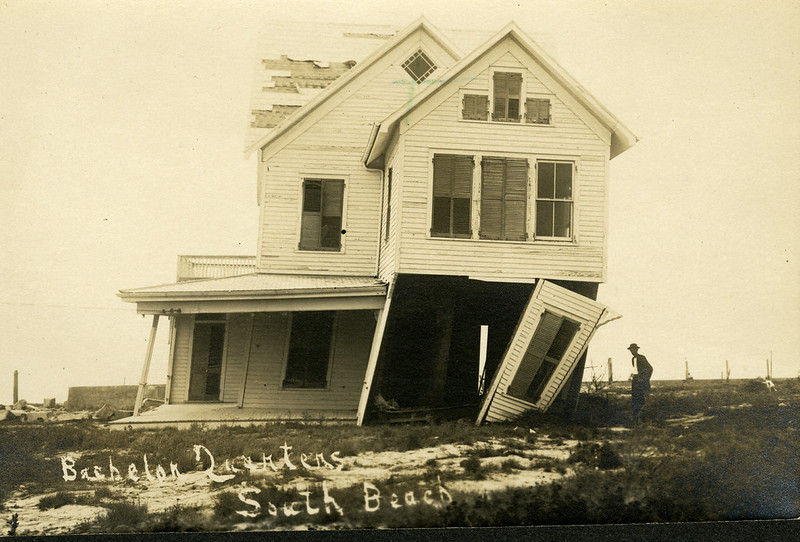 A damaged house listing to one side. Writing on photo reads Bachelor Quarters, South Beach