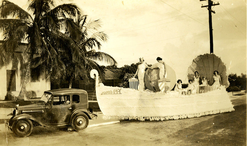 A 1920s style car pulling a float with people riding on it.