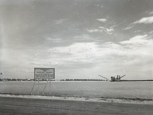 A sign that reads landfill for Capehart Housing on a shoreline with a dredge offshore