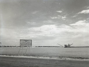 A sign that reads landfill for Capehart Housing on a shoreline with a dredge offshore