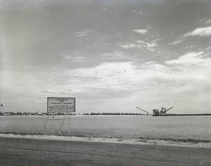A sign on a shoreline reading Landfill for Capehart Housing and a dredge offshore

