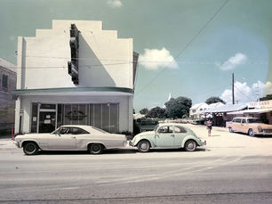Two cars in front of a building with an awning and a marquee sign.
