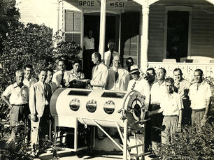 Group of men in suits gather around a cylindrical medical device outside a building labeled "BPOE No 551."