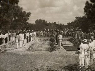 A large group of people at a mass bureual with three rows of caskets being interred.
