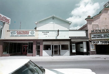 A street front with an electronic service center on the left and a theater on the right.