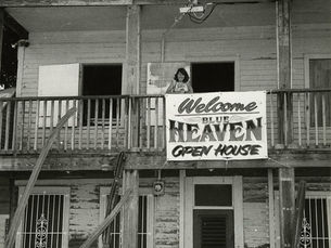 A woman standing on the upstairs porch of a house with a sign that reads Welcome Blue Heaven Open House