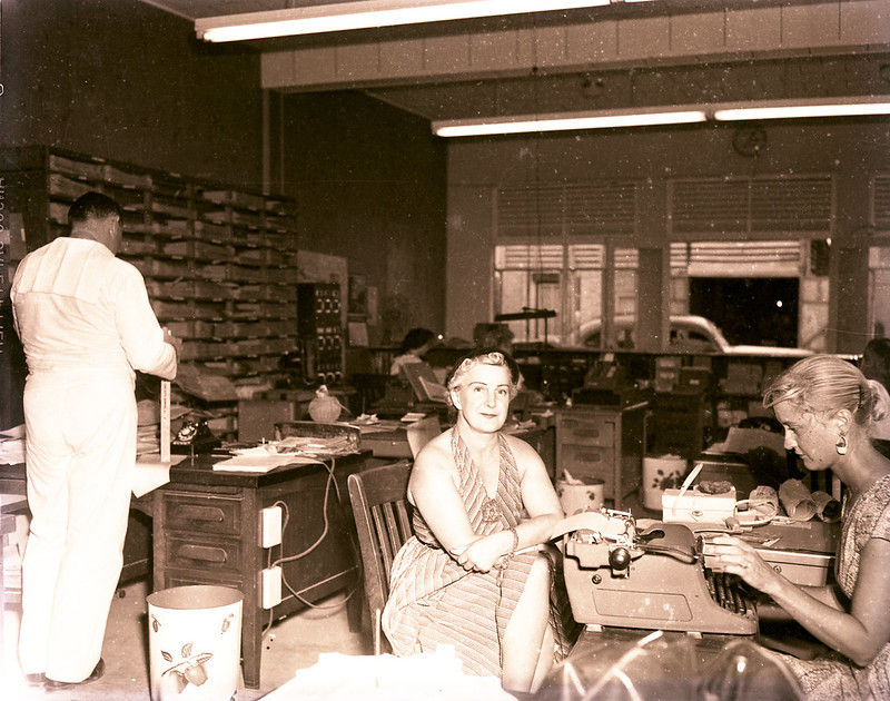 People in an office with a typewriter on a desk.