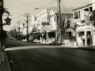 A street with businesses with signs that read House of Charm, Army Navy and Bahama Club