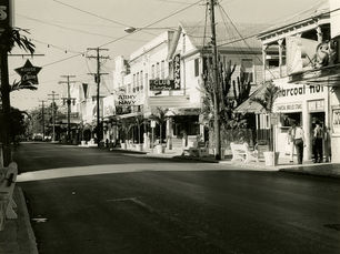 A street with businesses with signs that read House of Charm, Army Navy and Bahama Club