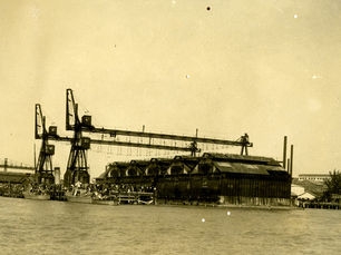 a crowd of people on a waterfront area with large sheds and gantries