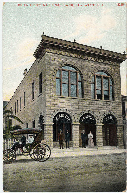 People in the entranceway and sitting in a carriage in front of a building with signs that read Island City National Bank.