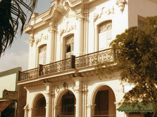 A baroque style building with three arched entryways on the ground fllor and a balcony on the second floor