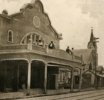 A building with men standing on a balcony over the street.