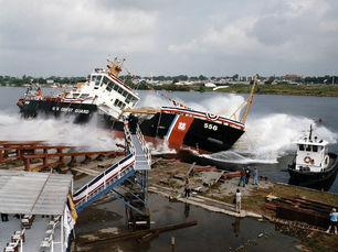 A Coast Guard cutter splashes into the water from a dock.