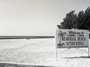 A beach with a sign that reads Welcome to Clarence S. Higgs Memorial Beach. No intoxicating beverages or dogs allowed on this beach.