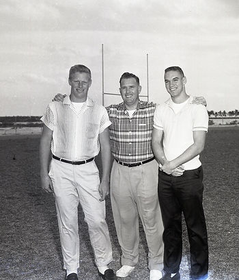 Three men on a field with goalposts behind them.