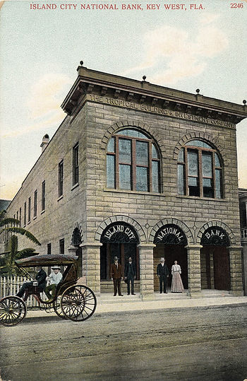 Post card of people standing and sitting in a buggy in front of a building with signs reading Island City National bank in the doorway arches.