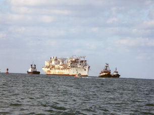 A large ship on the water with tugboats around it
