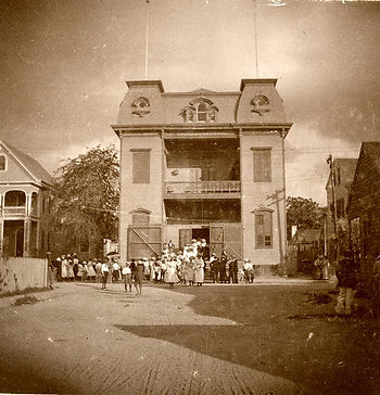 A group of people in front of a three story building with a mansard roof.