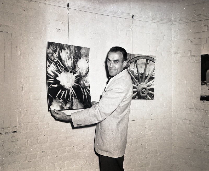 A man holds a photo handing on a wall.