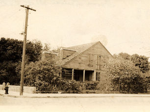 A small house with dormers and overgrown vegetation