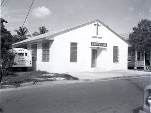 A building with windows in the shape of a cross over the door and signs that read Jesus Saves and Church of God.