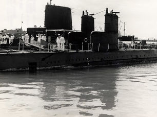 Submarines at a dock with sailors on board and on shore.