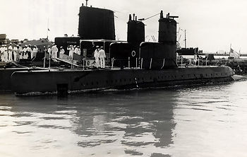 Submarines at a dock with sailors on board and on shore.