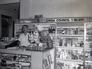Man standing at a magazine and snack stand labeled "Florida Council for the Blind."
