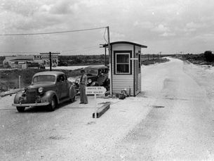 Two 1930s style cars and a person in a uniform at a tollboth with a sign that reads drive to the right.