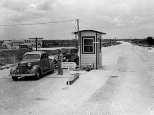 Two 1930s style cars and a person in a uniform at a tollboth with a sign that reads drive to the right.