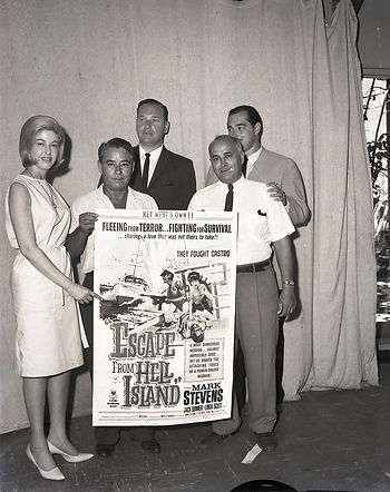 A group of people holding a poster that reads Escape From Hell Island.
