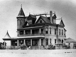 A three story house with a turret in one cornerith a ship called Key West in the background.