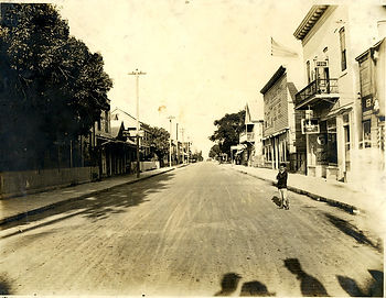 a boy stands in a street with stores on either side.