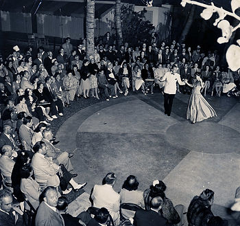 Two people dancing on a plaza with rows of people seated at the border.