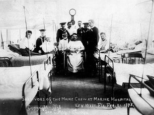 A group of men, some in Navy uniforms, in a hospital ward. Text on photo reads Survivors of the Maine Crew at Marine Hospital, Key West Fla. Feb. 21. 1898. Copyright 1898 Geo. C. Mages, Chicago.