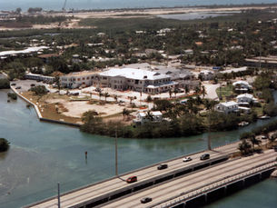 Aerial view of a building on a shoreline with a bridge in the foreground.