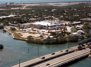 Aerial view of a building under construction on a shoreline with a separated bridge in the foreground.