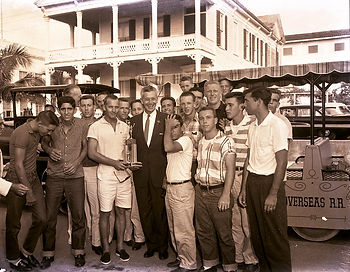 A group of young men with an older man, one of them holding a trophy.
