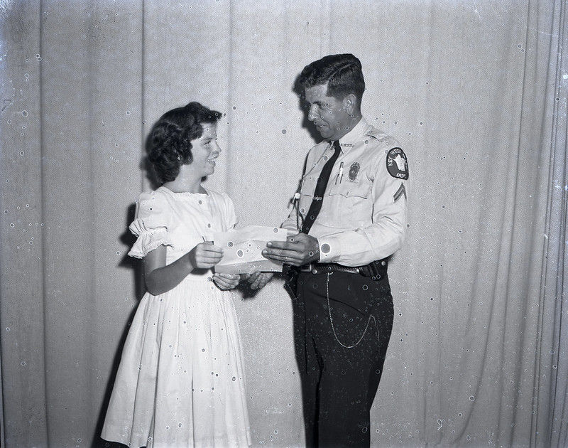 A man in a police uniform hands a piece of paper to a girl.