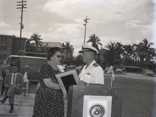 A woman accepts a plaque from a man in a Navy dress uniform