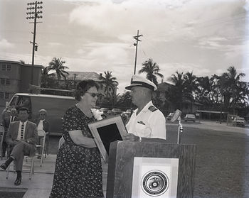 A woman accepts a plaque from a man in a Navy dress uniform.