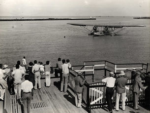 A group of people at a dock look at a seaplane on the water