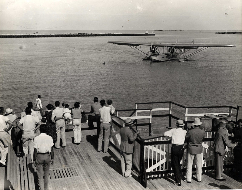 A group of people on a dock look at a seaplane on the water