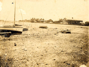 A beach with sailboats on shore and buildings in the background.